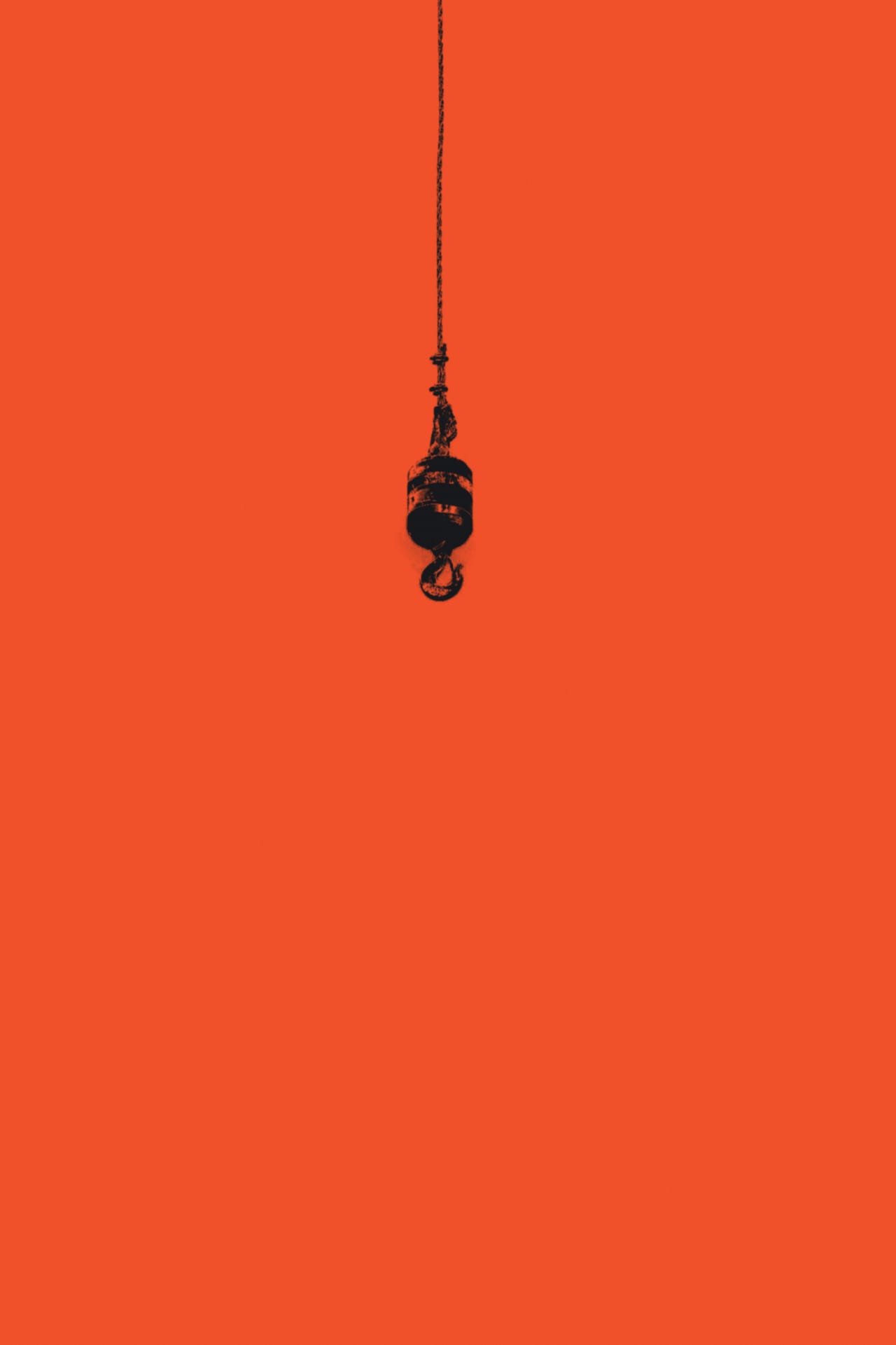 A single crane hook hanging in an empty orange field